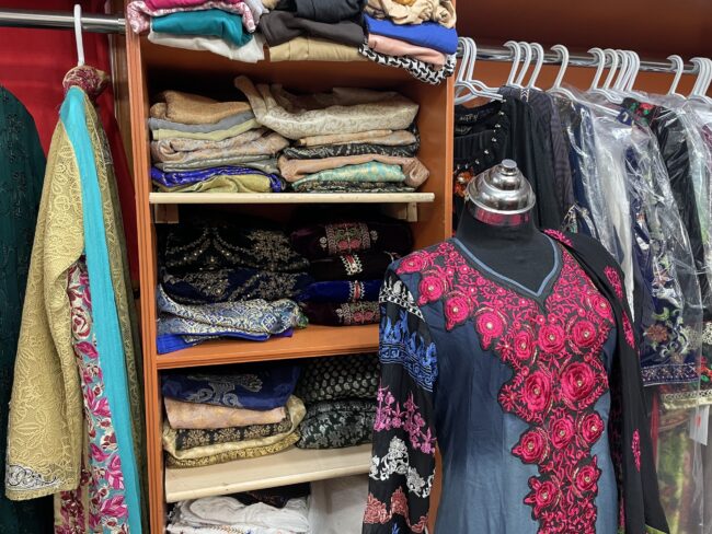 Closet filled with fabric with a black mannequin wearing a dress in front of it.