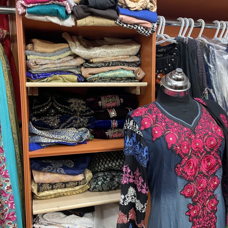 Closet filled with fabric with a black mannequin wearing a dress in front of it.