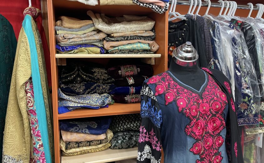 Closet filled with fabric with a black mannequin wearing a dress in front of it.