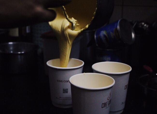 Egg coffee being poured into a paper cup. Two paper cups are beside it.