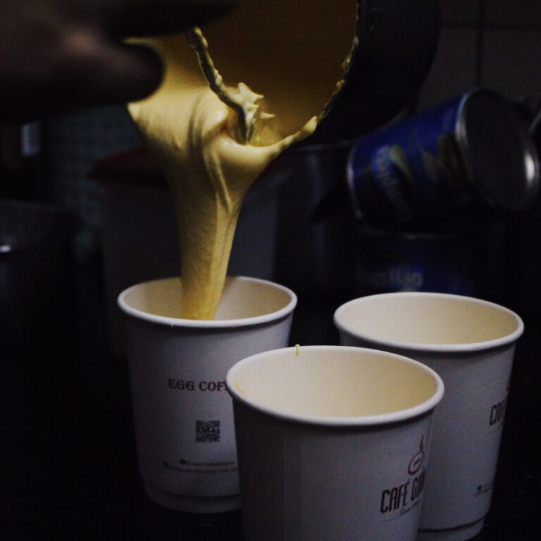 Egg coffee being poured into a paper cup. Two paper cups are beside it.