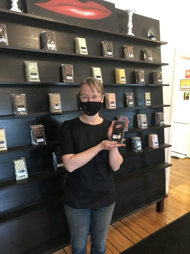 Woman holding wrapped chocolate in front of a display of chocolate.