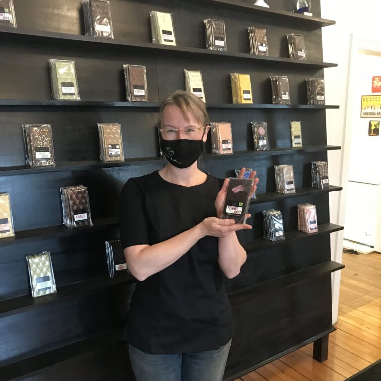 Woman holding wrapped chocolate in front of a display of chocolate.