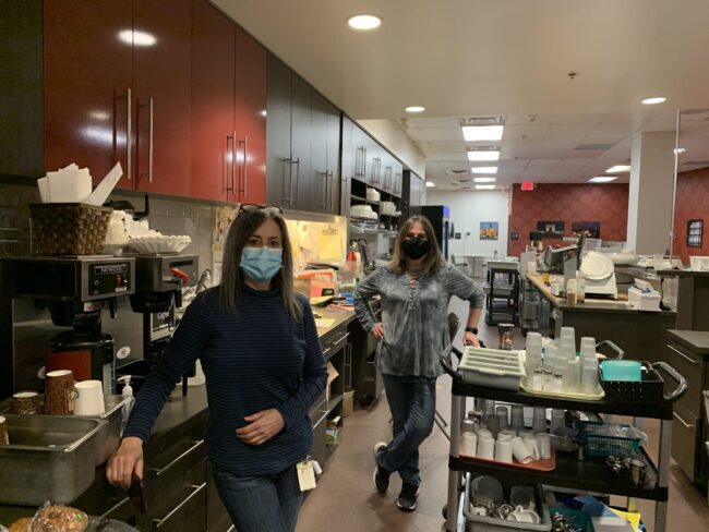 Two women in masks standing in a restaurant.