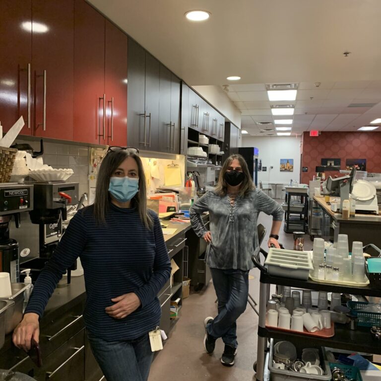 Two women in masks standing in a restaurant.