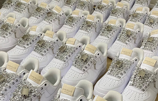 Multiple white shoes with it's shoelaces replaced with silver chains and a lock.