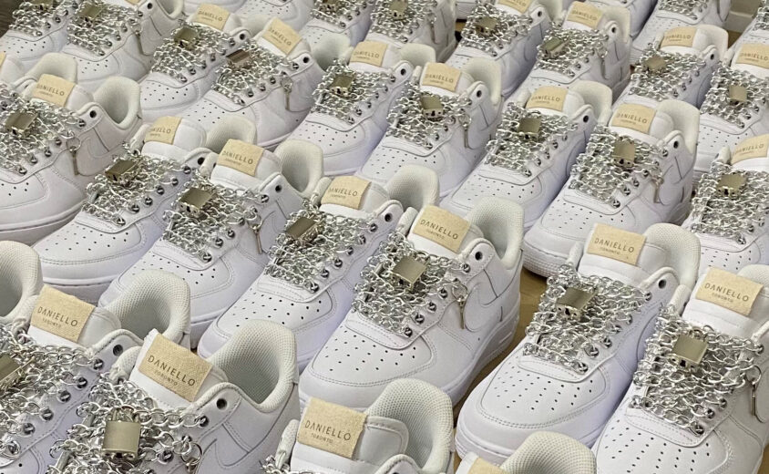 Multiple white shoes with it's shoelaces replaced with silver chains and a lock.