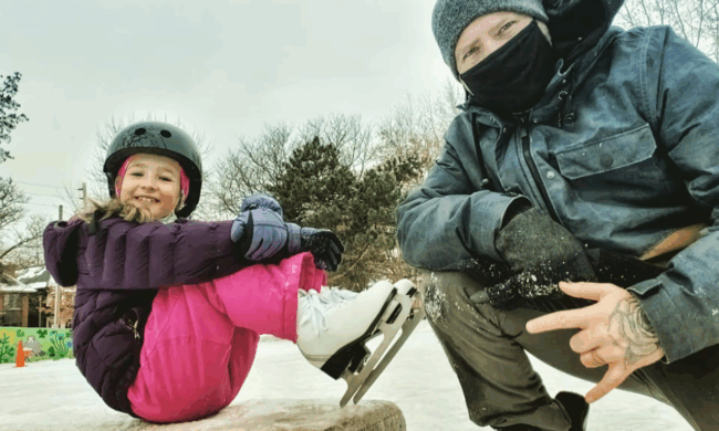 Young child in skates sitting on a rock next to a man.