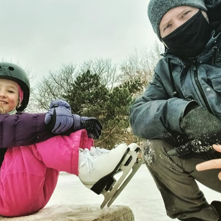 Young child in skates sitting on a rock next to a man.
