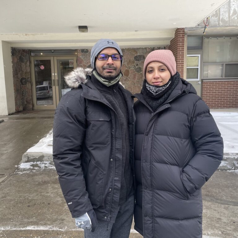A man wearing a dark coat on the left standing next to a women wear a dark coat on the right.