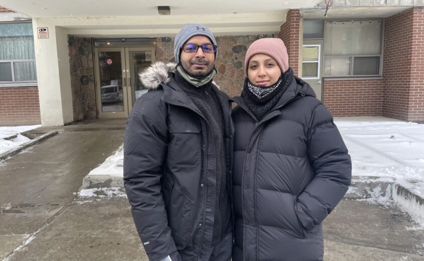 A man wearing a dark coat on the left standing next to a women wear a dark coat on the right.
