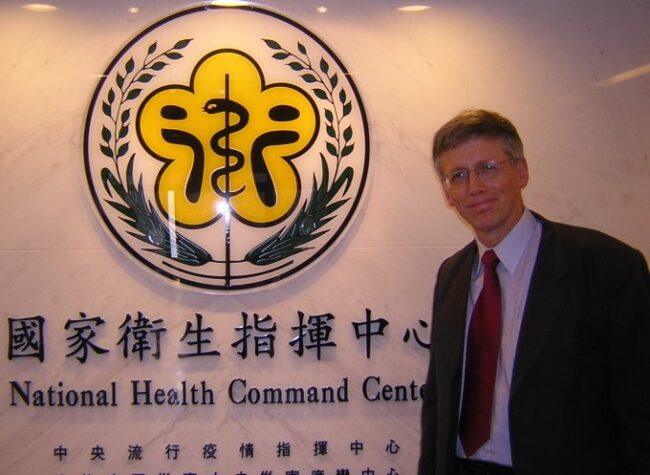 Man in a suit in front of the National Health Command Centre logo.