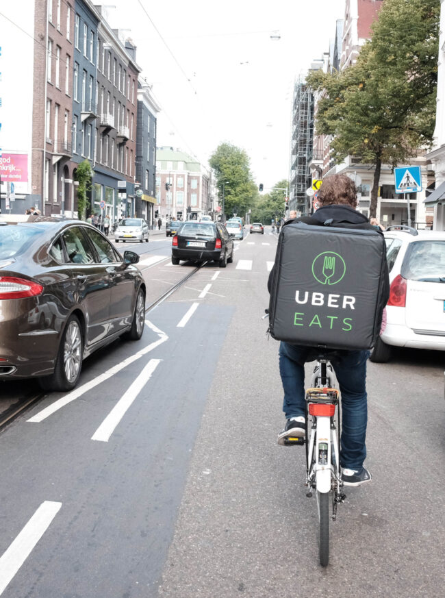An Uber Eats courier on a bike surrounded by traffic. He has a Uber Eats delivery backpack on.