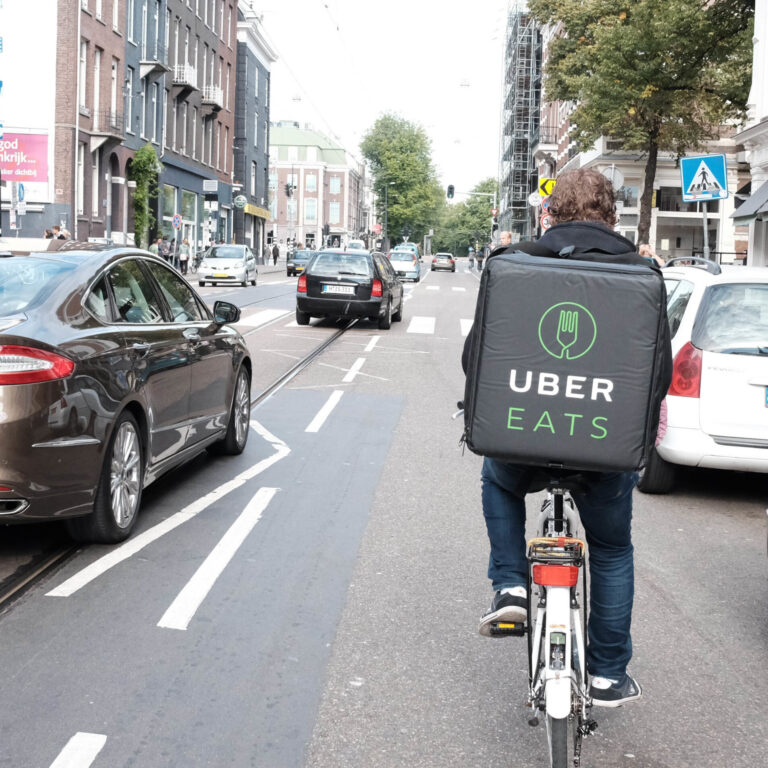 An Uber Eats courier on a bike surrounded by traffic. He has a Uber Eats delivery backpack on.