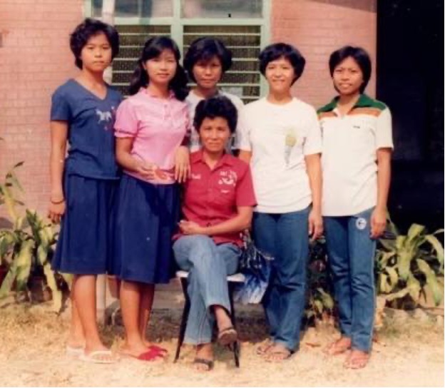 A family posing for a photo outside of their home in Alaminos, Philippines. One person is sitting while five people stand behind them, smiling. 