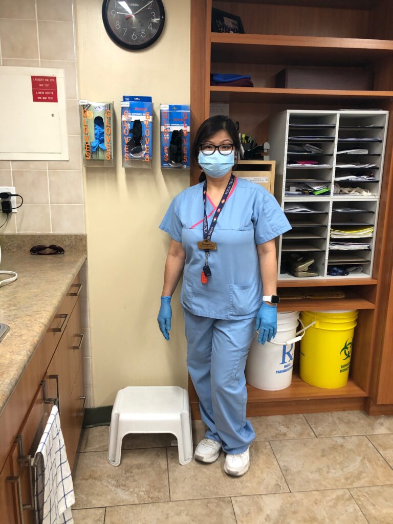 A personal support worker poses for a photo wearing scrubs, a face mask and gloves at a retirement home.