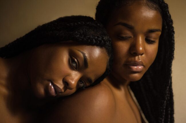 A black woman lying her head on the shoulder of another black woman.