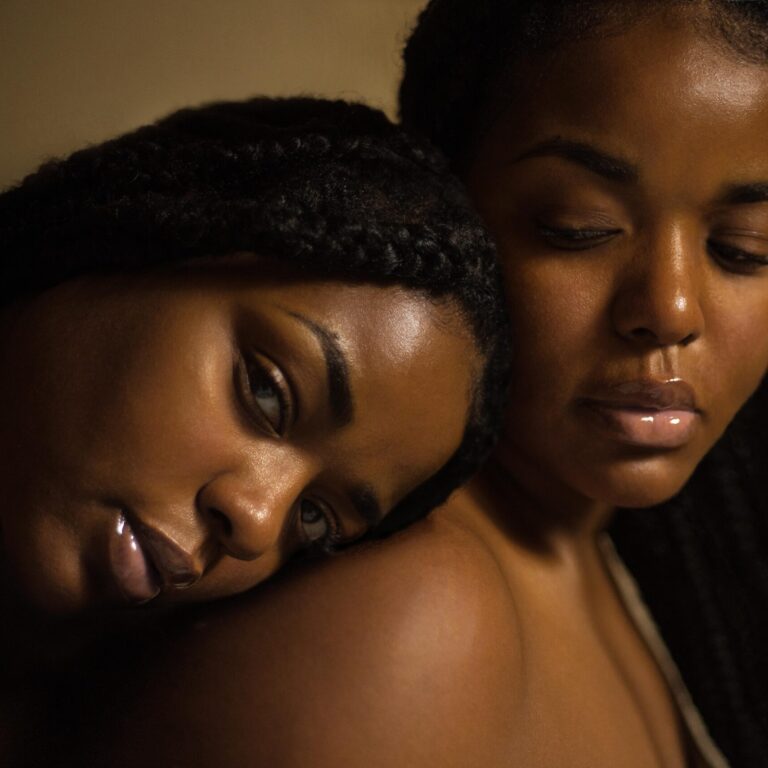 A black woman lying her head on the shoulder of another black woman.