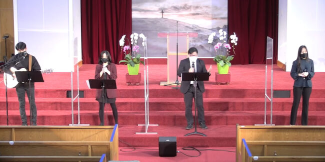 Band in black clothing performing on stage with transparent partitions between them.