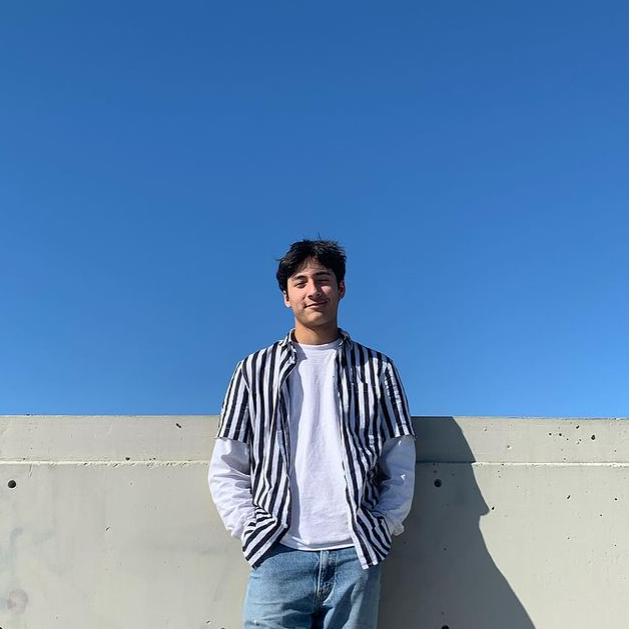 Man in a striped jacket leaning against concrete wall.