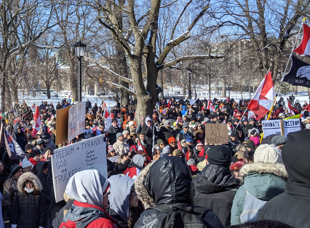 A huge crowd of people holding signs and marching in the same direction underneath the snow covered trees in a park during the winter.