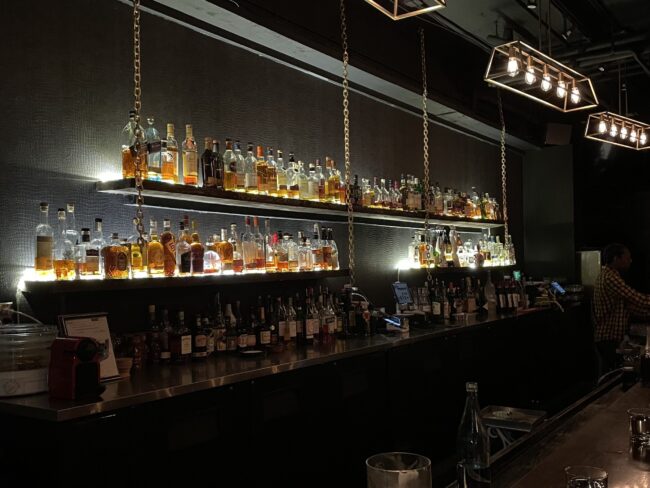 Back of bar, lit up shelves with bottles of liquor