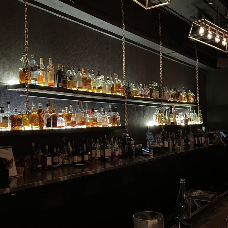 Back of bar, lit up shelves with bottles of liquor