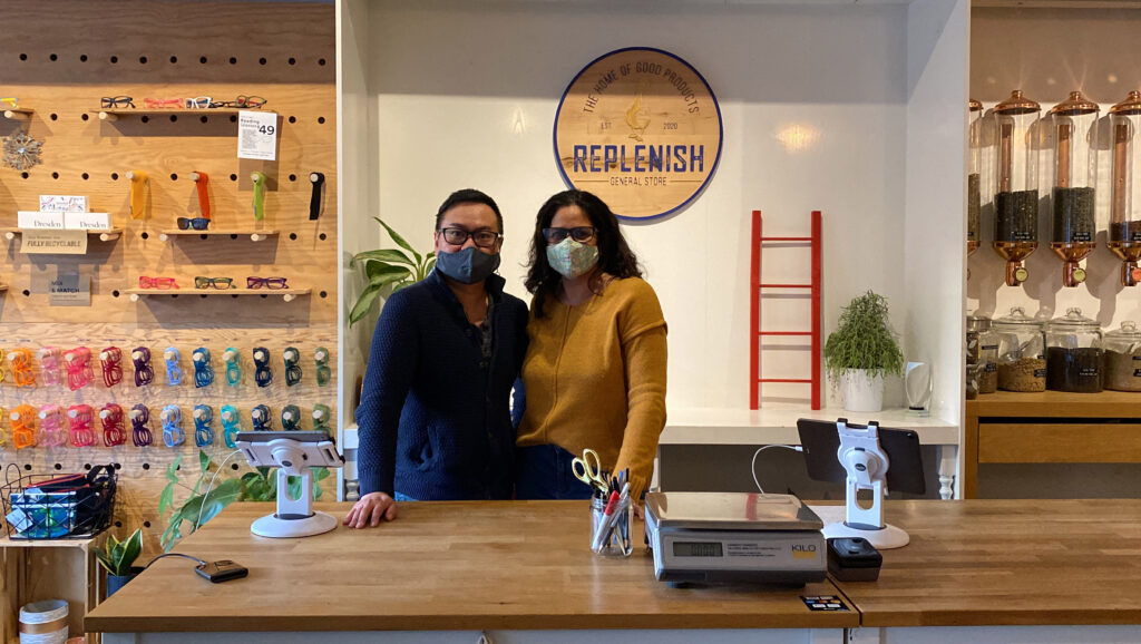 Thai Pham and Bianca Martins stand in front of a sign that says, "Replenish General Store."