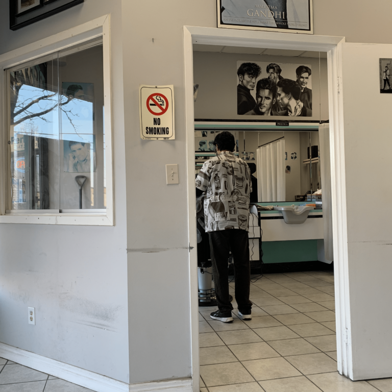 A man cuts hair in a small barbershop.