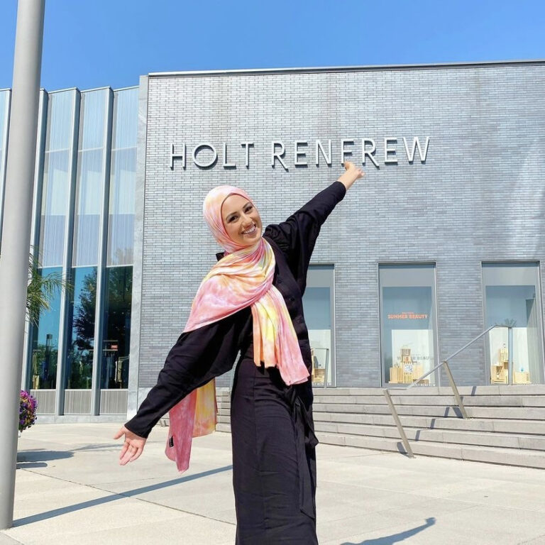 Woman excitedly posing in front of a building labelled "Holt Renfrew"