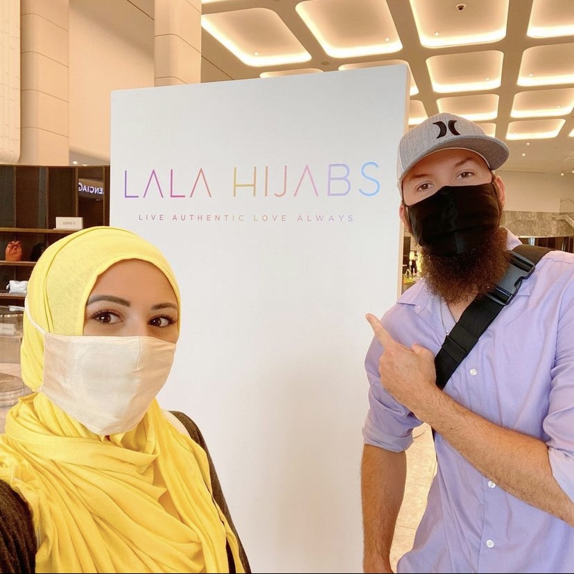 Couple standing in front of a sign branded "Lala Hijabs."