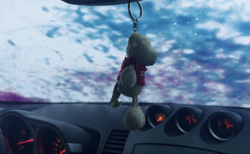 Image of a small keychain teddy bear hanging from the rearview mirror of a Nissan 350Z. Interior shot.