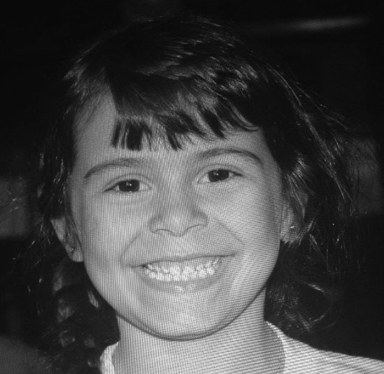Aeva Alexandrovich smiling brightly into the camera at seven years old in 2011.