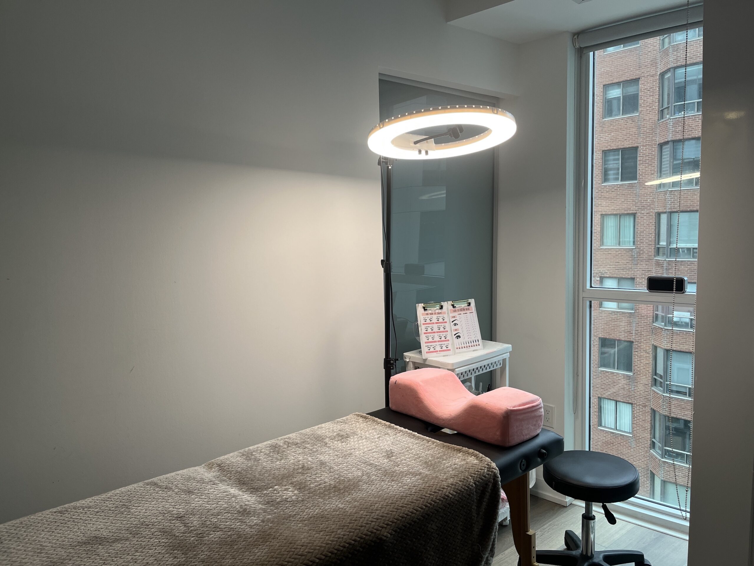 A massage table with a pink neck pillow and an overhead ring light.