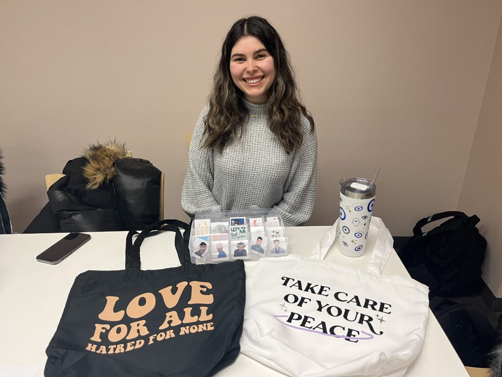 Young woman sits behind a table showcasing different products.