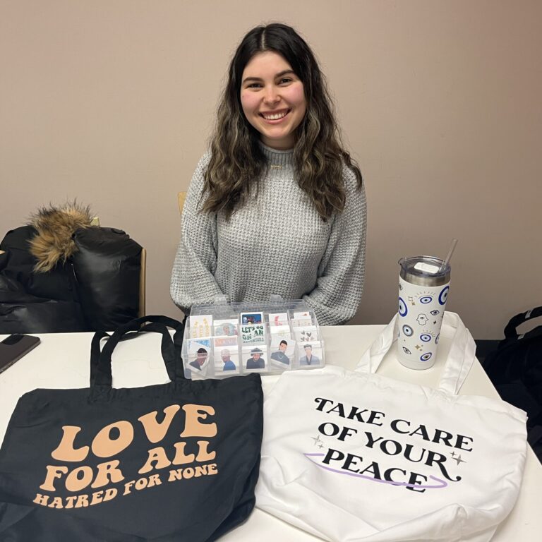 Alvarez12 Young woman sits behind a table showcasing different products.