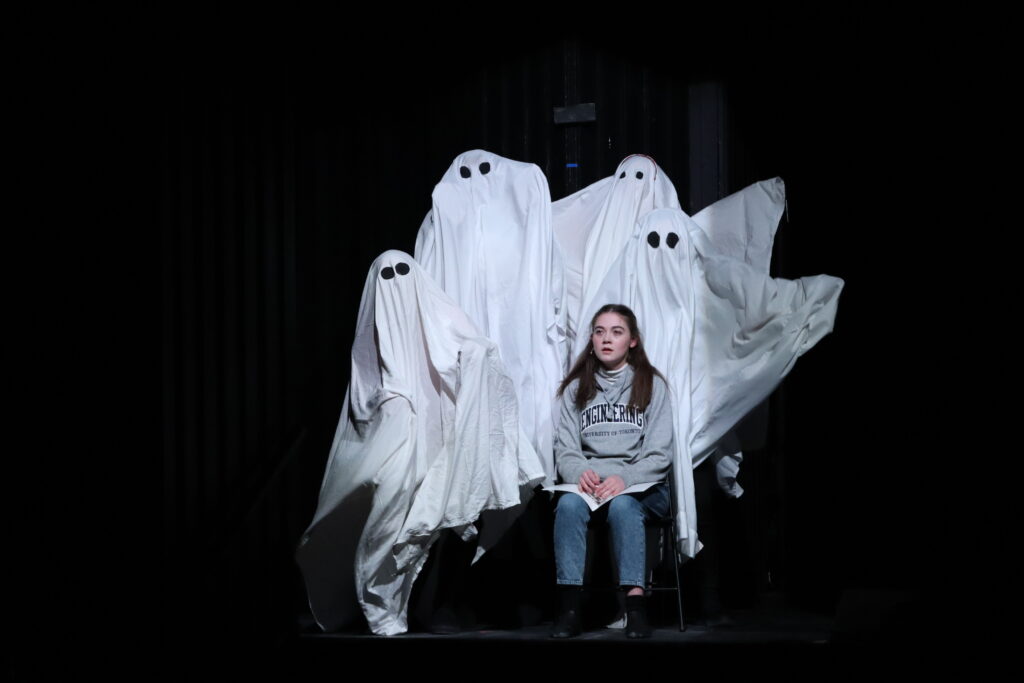 A woman sits surrounded by five people in ghost costumes.