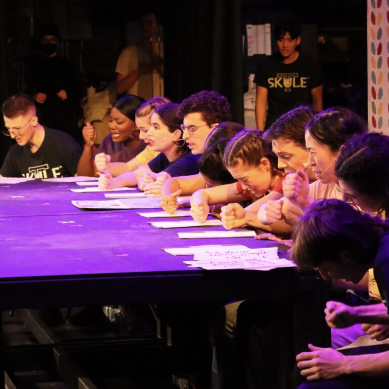 Students sitting at a table under colourful lights looking confused and stressed.