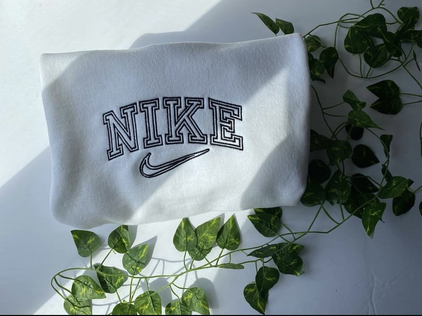 White sweater with Nike written on it, green leaves around it.