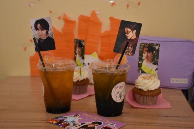 Two cups filled with juice on top of a wooden table with photographs of Jung Hoseok from BTS displayed along decorative birthday-themed postcards