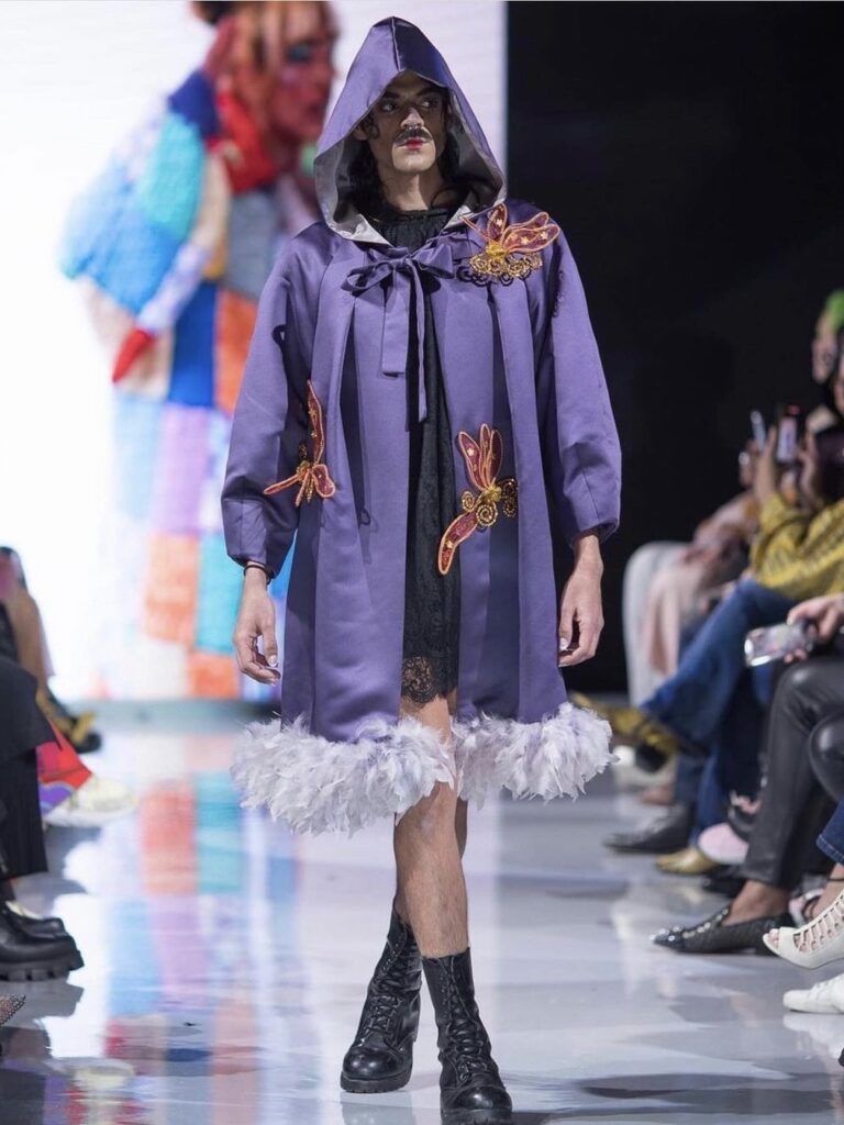 Model walks down the runway in a sleek purple cloak