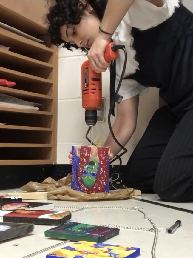 A designer using a power drill on a painting canvas.