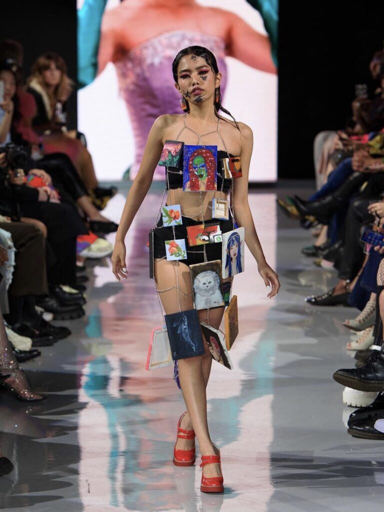 The model walks down the runway wearing the draped paintings garment.