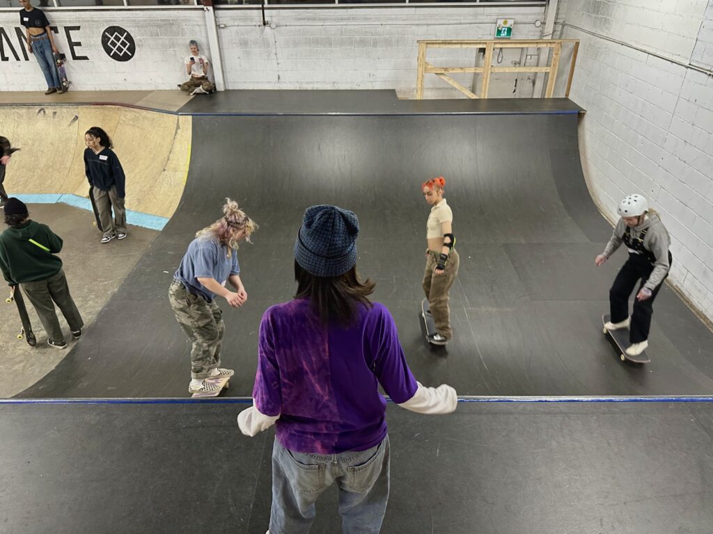 Michaela standing on skate ramp while girls practice skills