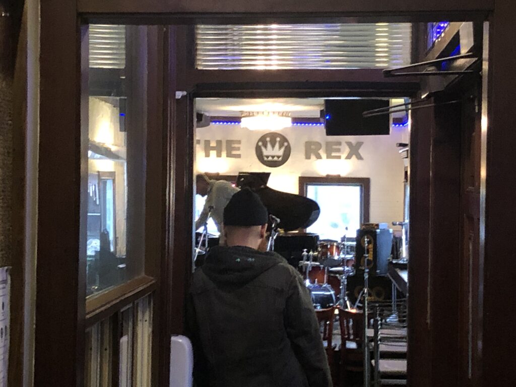 A man in a toque stands in a doorway facing the stage at The Rex Hotel Jazz and Blues Bar