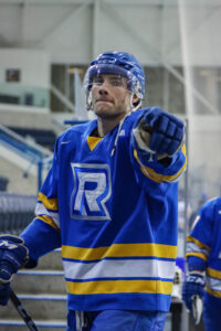 Hockey player walking away from the ice holding a hockey stick and pointing at the camera with his glove
