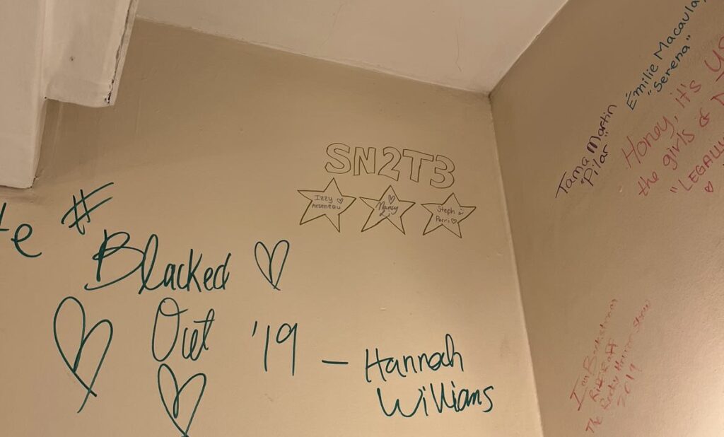 Writing on a wall saying "Skule Nite 2T3" with 3 names in hearts underneath it.