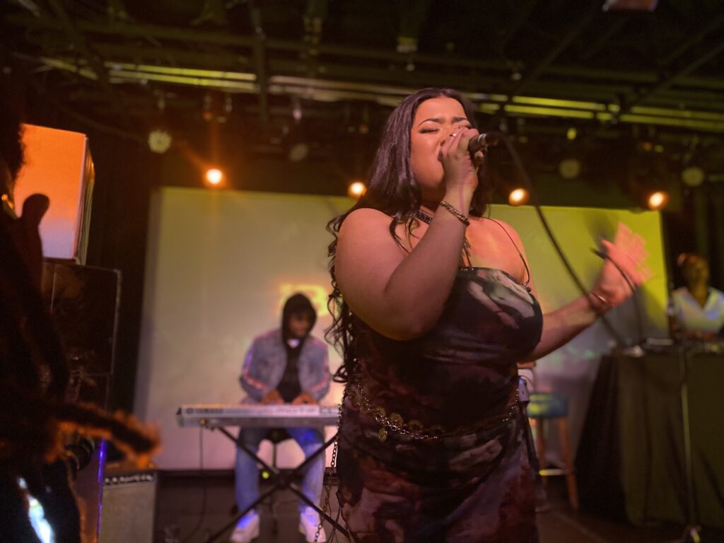 Toronto based singer, Benita on stage in a mosaic dress singing passionately with her eyes closed.