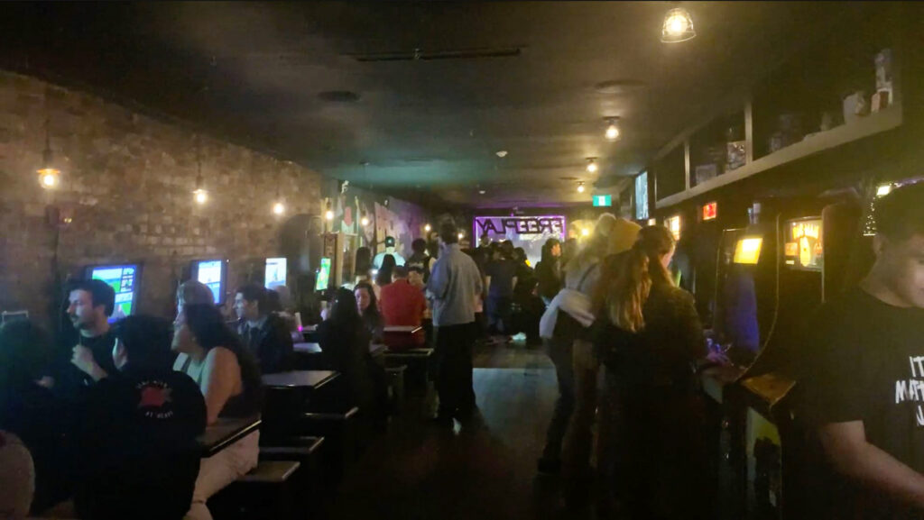 Crowds of people gathering and mingling in an arcade and eatery setting.