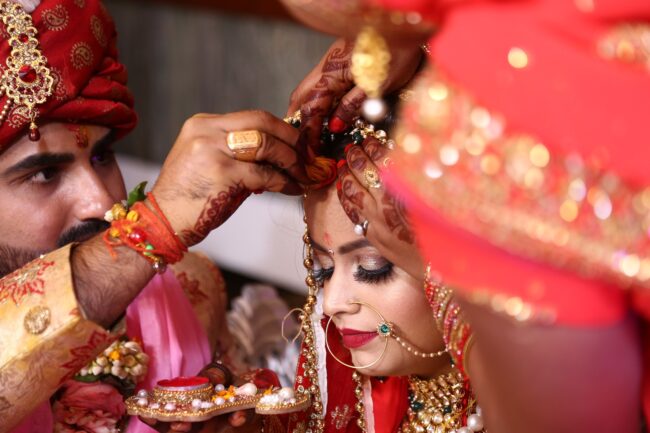 An Indian wedding featuring a husband and wife wearing red traditional Indian clothes.